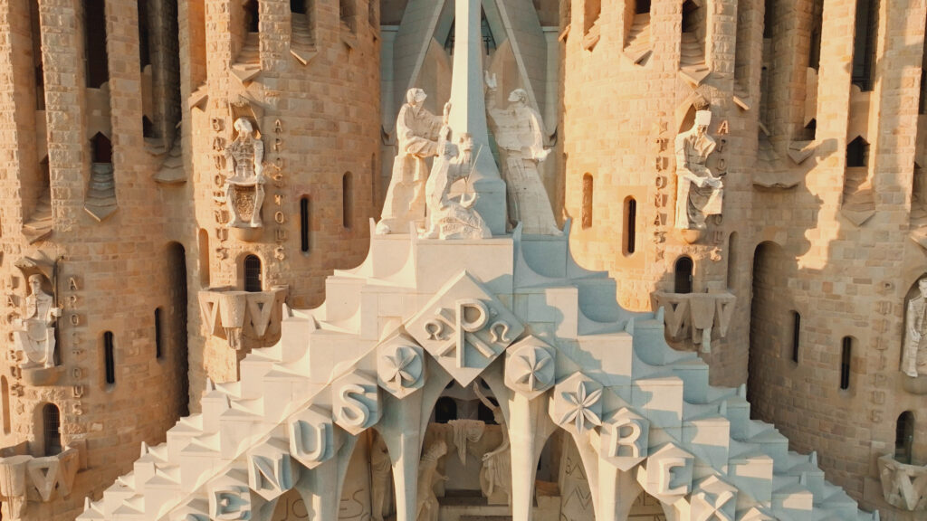 PERNEL_MEDIA_ANCSUP2_SAGRADA_11 - viasathistory.eu Close-up of a sculpted stone façade with statues and geometric details bathed in warm light, likely part of the Sagrada Família complex in Barcelona.